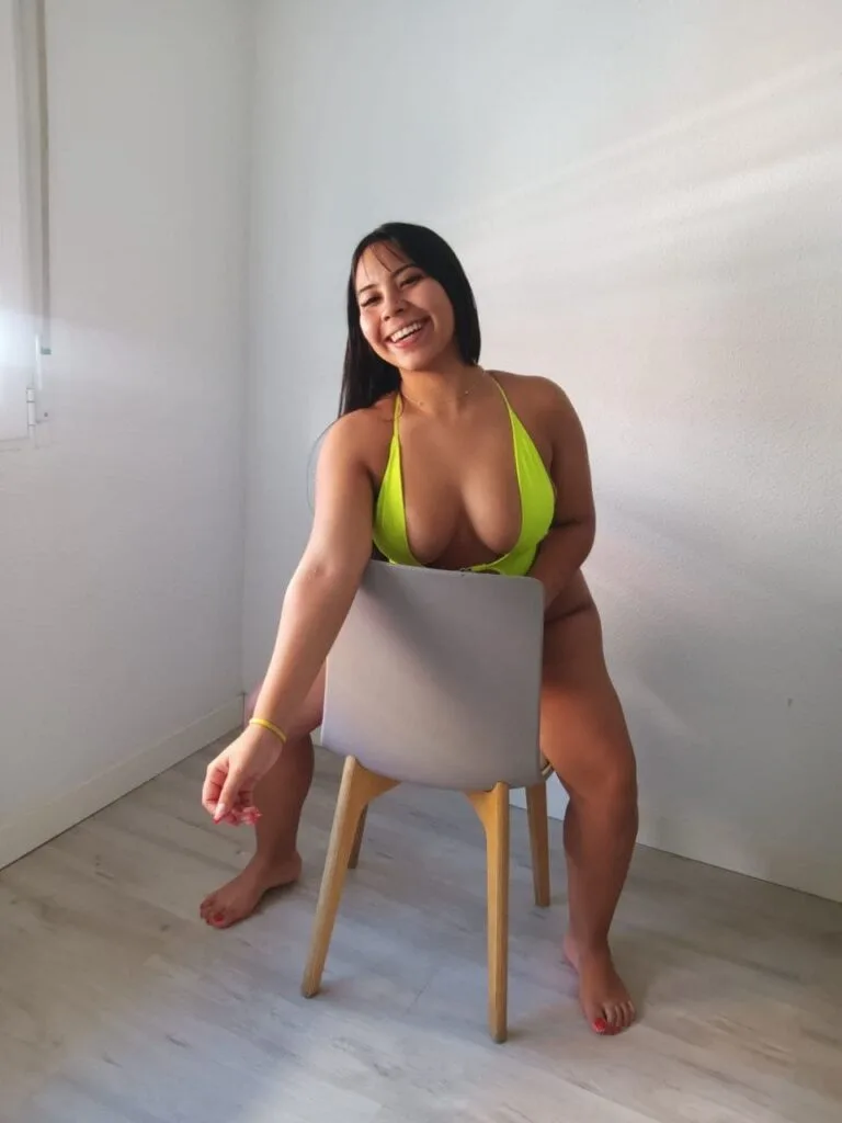 Nathy, puta de 22 años posa sonriendo sentada en una silla gris en Malaga